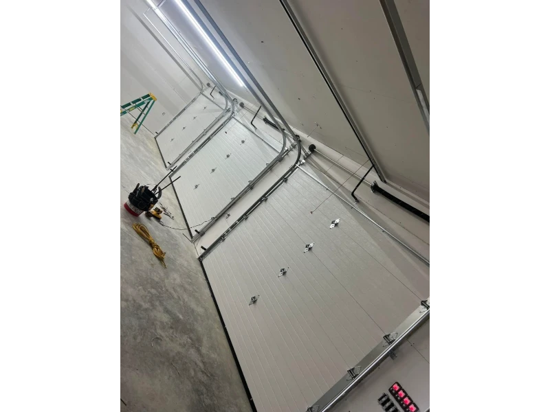 Commercial overhead door installation in a large bay with lift, tracks, and tools visible.