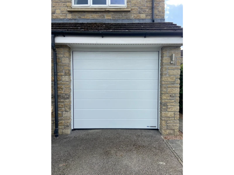 White sectional overhead door installed on a stone garage exterior.