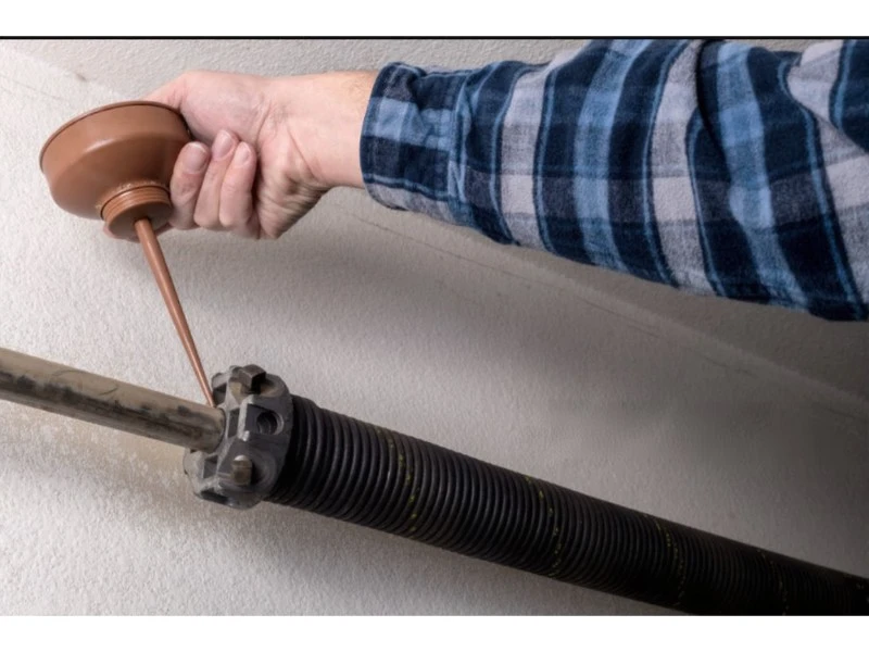 Applying lubricant to a torsion spring after garage door spring repair in Alvin, TX to reduce noise.