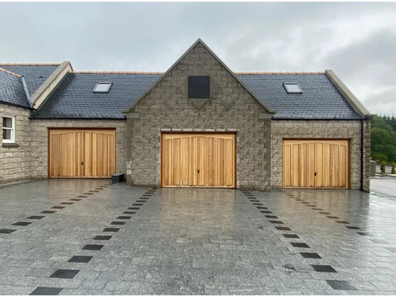 Wood-style garage doors installed on a stone garage—warm, premium look (Alvin, TX).