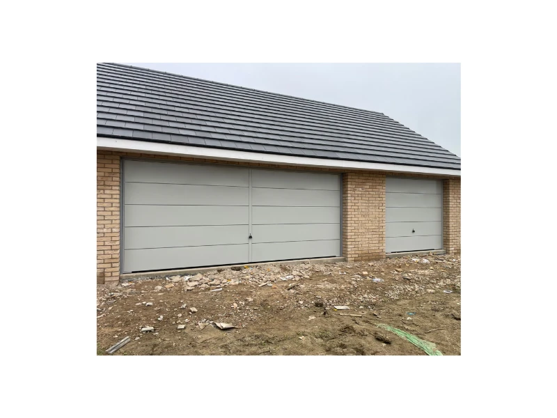 Flush-panel gray garage doors installed on a new construction garage (Alvin, TX).